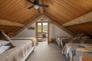 A cozy attic bedroom with two beds, a ceiling fan, and a balcony with a view.