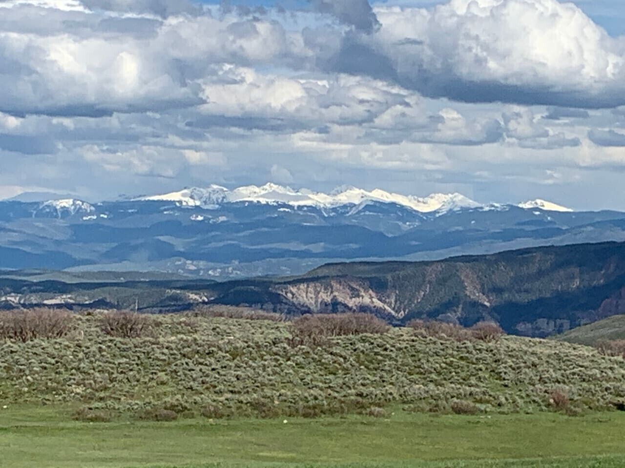 Un paysage montagneux avec des pics enneigés à l’horizon et une étendue herbeuse au premier plan.