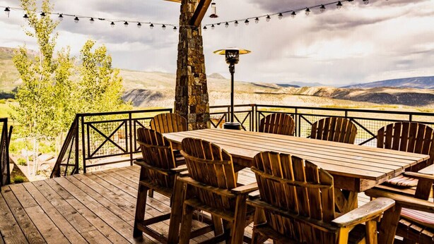 Une terrasse en bois avec une table et des chaises, offrant une vue sur un paysage montagneux.
