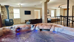 Un salon spacieux avec une cheminée en pierre, un grand téléviseur et un jacuzzi en premier plan.