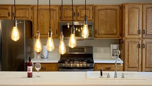 Une cuisine dotée de meubles en bois, d’un réfrigérateur en acier inoxydable, d’un four encastré et d’un luminaire suspendu avec des ampoules apparentes.