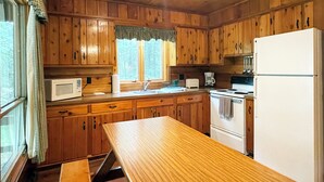 A wooden cabin kitchen with a wooden table, a refrigerator, a stove, and a microwave. - Charming 2 Bedroom Cabin in the Poconos on Private Resort (Stroudsburg)