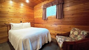A wooden cabin room with a bed, a chair, and a window with curtains. - Charming 2 Bedroom Cabin in the Poconos on Private Resort (Stroudsburg)