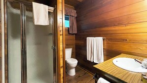 A wooden cabin bathroom with a glass shower door, a toilet, and a wooden vanity with a sink. - Charming 2 Bedroom Cabin in the Poconos on Private Resort (Stroudsburg)