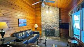 A cozy cabin interior with wooden walls, a stone fireplace, leather sofas, and a television. - Charming 2 Bedroom Cabin in the Poconos on Private Resort (Stroudsburg)