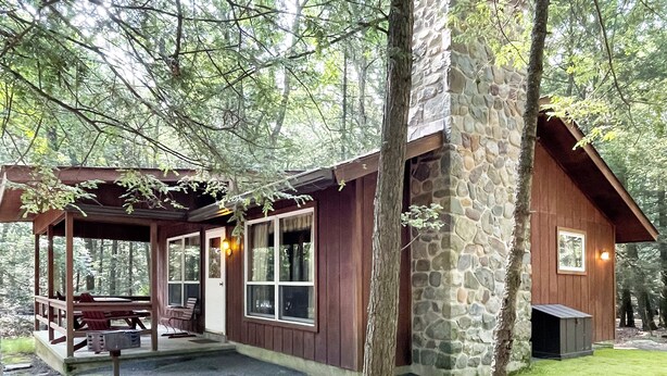 A cabin with a stone exterior, wooden deck, and a covered patio area. - Charming 2 Bedroom Cabin in the Poconos on Private Resort (Stroudsburg)