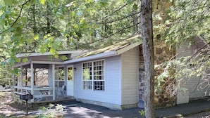 A small cabin with a porch, a stone wall, and a covered outdoor seating area.