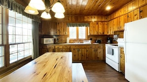 A wooden cabin kitchen with a large wooden table, a stove, a microwave, and a refrigerator.