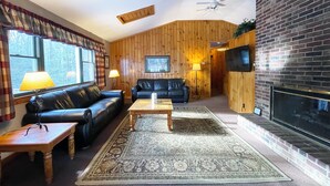 Ein gemütliches Wohnzimmer mit Holzwänden, einem Kamin, einer schwarzen Ledersofa, einem Couchtisch und einem gemusterten Teppich.