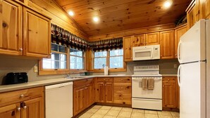 A kitchen with wooden cabinets, a microwave, a stove, and a refrigerator. - Luxurious Lake View Log Cabin with Fire Pit in the Poconos (Stroudsburg)