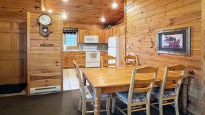 A wooden cabin interior with a dining table, chairs, a clock, and kitchen appliances. - Luxurious Lake View Log Cabin with Fire Pit in the Poconos (Stroudsburg)