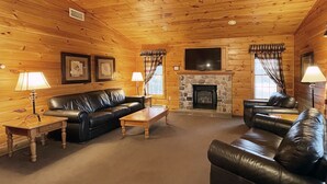 A log cabin interior with a stone fireplace, leather sofas, and wooden walls. - Luxurious Lake View Log Cabin with Fire Pit in the Poconos (Stroudsburg)