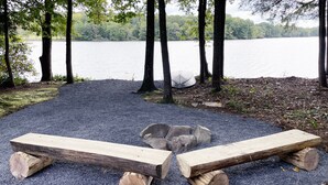 A gravel area with two wooden benches and a fire pit. - Luxurious Lake View Log Cabin with Firepit in the Poconos (Stroudsburg)