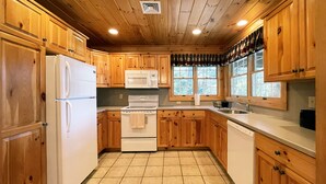 A kitchen with wooden cabinets, a refrigerator, a microwave, a stove, and a sink. - Luxurious Lake View Log Cabin with Firepit in the Poconos (Stroudsburg)