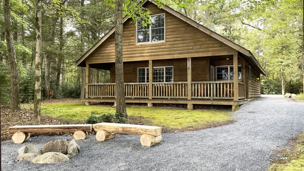 A wooden cabin with a porch, surrounded by trees. - Luxurious Lake View Log Cabin with Firepit in the Poconos (Stroudsburg)