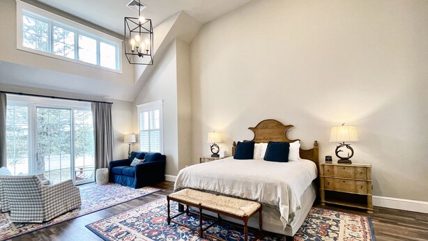 A spacious bedroom with a large bed, a bench, a blue armchair, and a nightstand with a lamp. - Romantic Couples Suite in the Poconos (Stroudsburg)