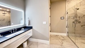 Een moderne badkamer met een wastafel met twee kommen, een grote spiegel en een douchecabine met glazen wanden.
