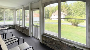 En overdækket veranda med stenvægge, store vinduer og udendørs møbler.