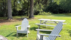 Un coin pique-nique aménagé avec deux chaises Adirondack et une table de pique-nique dans un espace verdoyant d’un parc.