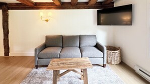 A modern living room with exposed wooden beams, a grey sofa, a wooden coffee table, a flat-screen TV, and a wall-mounted light fixture. - Poconos Rustic 1BR in the Poconos on Private Resort (Stroudsburg)