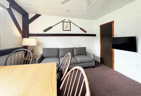 A room with a wooden dining table, a grey sofa, and a TV mounted on the wall. - Poconos Rustic 2BR in the Poconos on Private Resort (Stroudsburg)