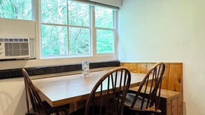 Ein Essbereich mit Holztisch und zwei Stühlen, ein Fenster mit Blick auf Bäume und eine Klimaanlage an der Wand.