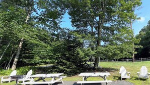 Ein Picknickplatz mit zwei Picknicktischen und vier Adirondack-Stühlen.