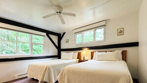 Ein Zimmer mit zwei Betten, einem Deckenventilator und großen Fenstern mit Blick auf Bäume.