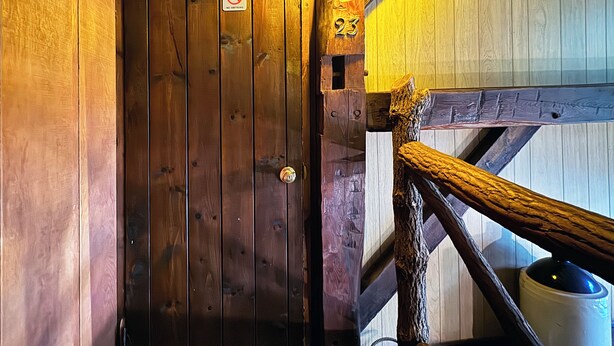 Eine Holztür mit einem 'Nichtraucher'-Schild, einer Nummer '23' und einer rustikalen Holztreppe mit einer Lampe.