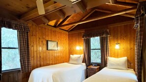 Quarto de cabana com duas camas, paredes de madeira e uma janela com cortinas.