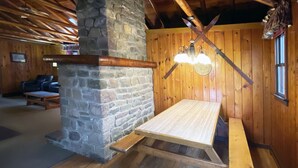 Um interior rústico em madeira com lareira de pedra, bancos de madeira e um ventilador de teto.