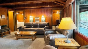 A cozy living room with a leather sofa, a wooden coffee table, and a lamp on a side table. - Charming Lake Front Log Cabin with Fire Pit in the Poconos (Stroudsburg)