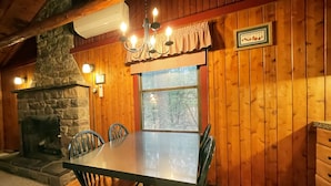 A cozy dining area with a stone fireplace, wooden walls, and a chandelier. - Charming Lake Front Log Cabin with Fire Pit in the Poconos (Stroudsburg)