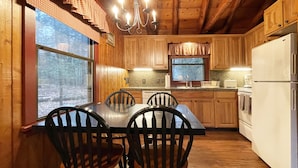 A wooden cabin kitchen with a dining table and chairs, a chandelier, and a refrigerator. - Charming Lake Front Log Cabin with Fire Pit in the Poconos (Stroudsburg)