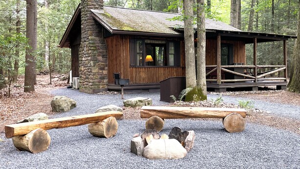 A rustic cabin with a stone chimney, wooden deck, and a fire pit area. - Charming Lake Front Log Cabin with Fire Pit in the Poconos (Stroudsburg)