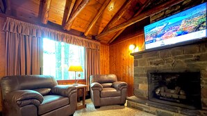 A cozy living room with a stone fireplace, leather sofas, and a television mounted above it. - Charming Lake Front Log Cabin with Fire Pit in the Poconos (Stroudsburg)