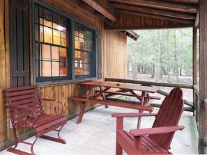 A wooden cabin with a covered porch, picnic table, and Adirondack chairs. - Charming 3 BR Log Cabin in the Poconos (Stroudsburg)