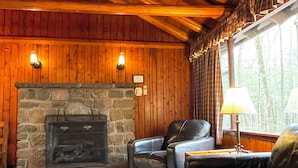 Um quarto aconchegante com lareira de pedra, poltronas de couro e uma janela com cortinas.