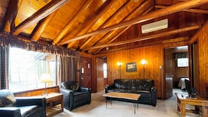 Um quarto com painéis de madeira, um sofá, duas poltronas, uma mesa de centro e um abajur.