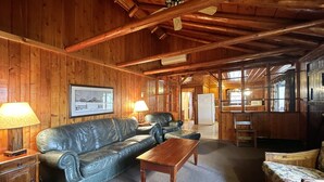Interno di una baita in legno, con un divano in pelle, un tavolino in legno e un quadro appeso al muro.