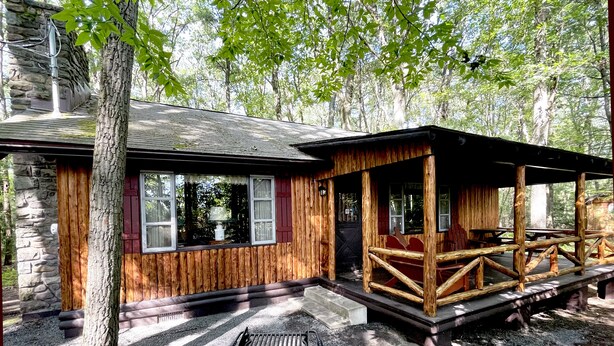 Un rustico chalet con fondamenta in pietra, pareti in legno e un portico con posti a sedere.