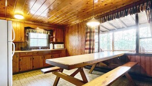 Una baita in legno con angolo cottura, un tavolo da pranzo con panche e una finestra con tende.