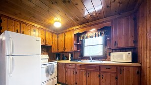 Una cucina con mobili in legno, un frigorifero bianco, un fornello, un forno a microonde e una finestra con tende.