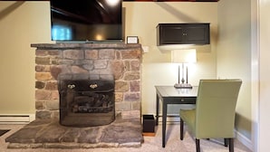 A stone fireplace with a TV above it, a lamp on a table, and a chair.