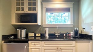 A kitchen with white cabinets, a stainless steel refrigerator, a microwave, and a window with a view of trees.