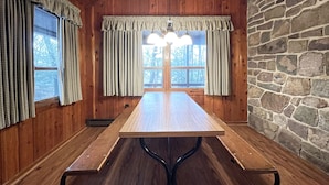 Una mesa de madera para comer con una pared de piedra y ventanas con cortinas.