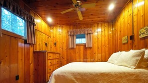 Un dormitorio con paneles de madera, una cama, un aparador y un ventilador de techo.