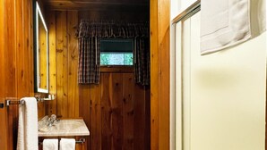 Un baño de madera con lavamanos, espejo y ventana.