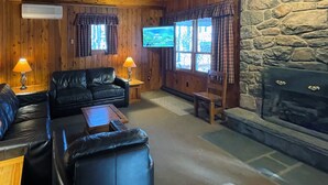 Interior acogedor de una cabaña con chimenea de piedra, paredes de madera, sofá de cuero y televisor.