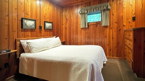 Un dormitorio con paneles de madera, una cama, un aparador y dos cuadros en la pared.
